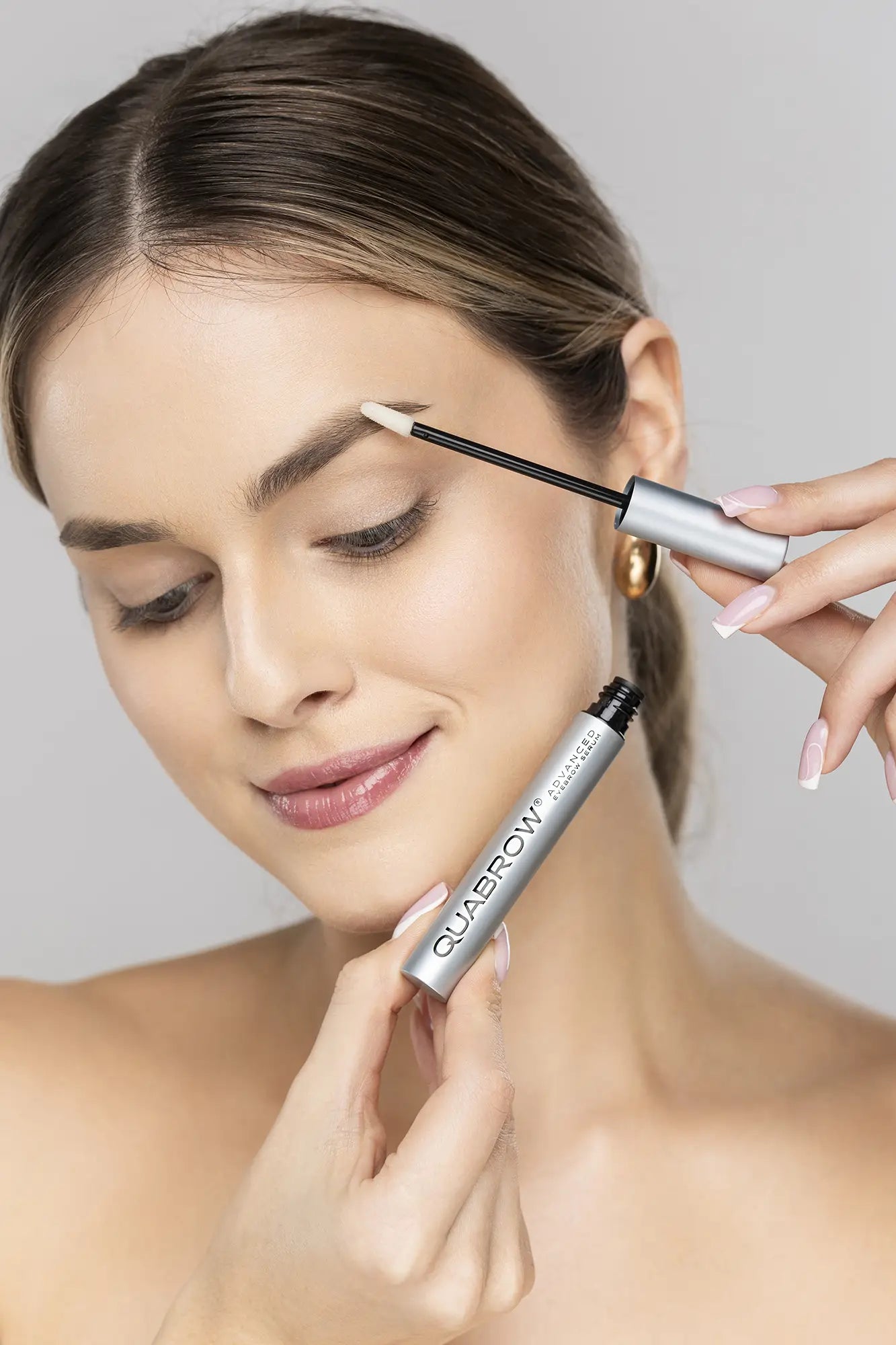 Blond kvinde påfører QUABROW Advanced Eyebrow Serum på sine øjenbryn med applikatoren – trin for trin-brug