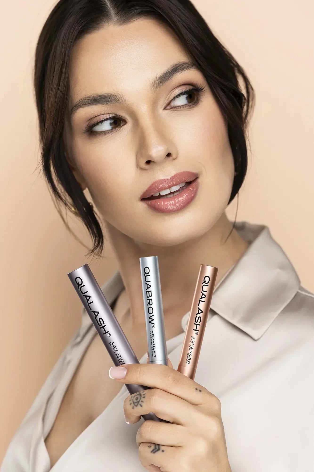 Femme tenant trois produits QUALASH & QUABROW face à l’objectif – soin des cils et des sourcils