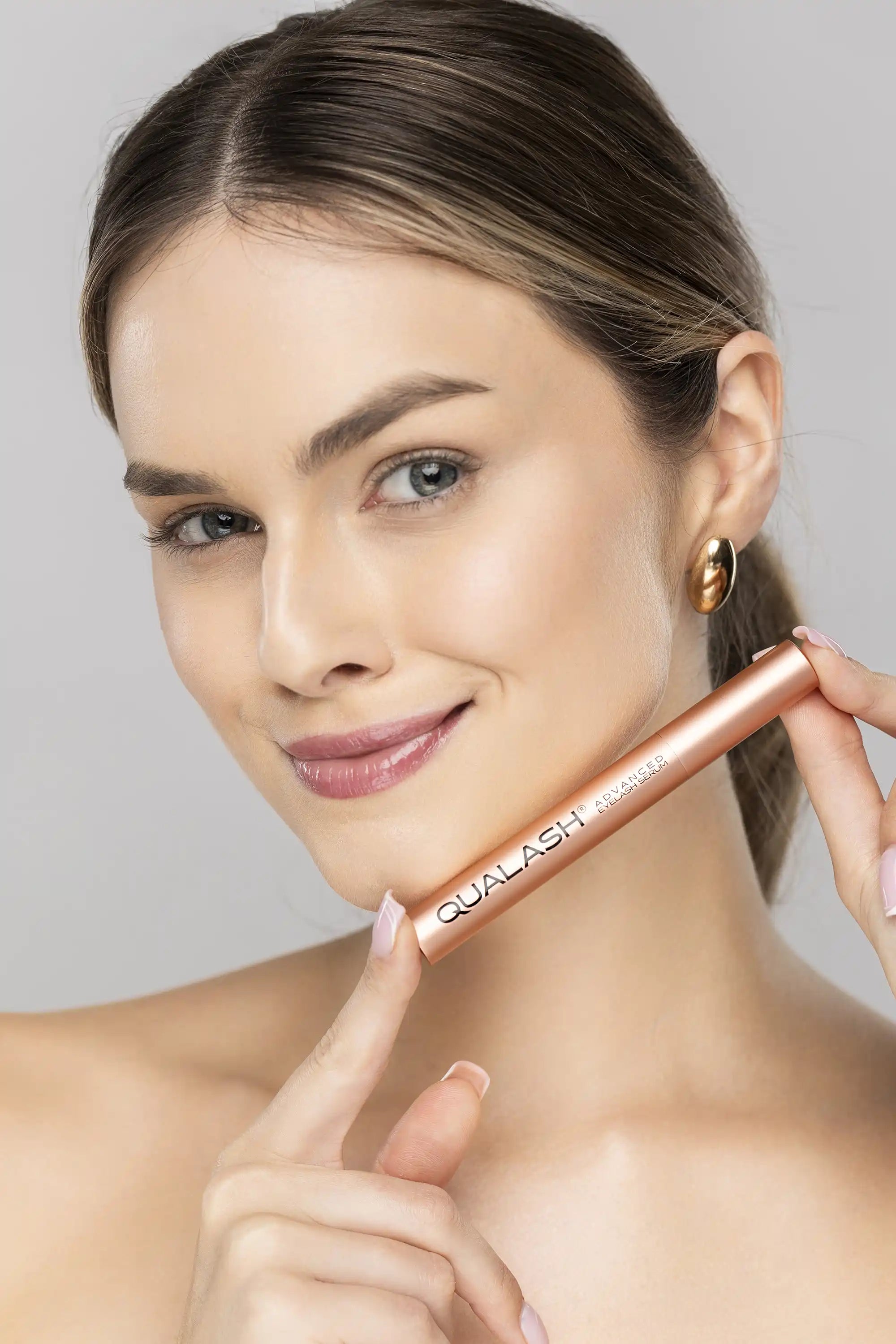 Femme souriante tenant le sérum avancé pour cils QUALASH avant application