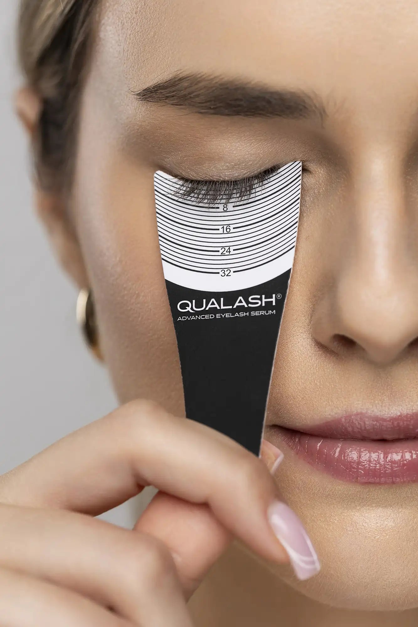 Close-up des cils mesurés avec une règle pour cils arborant le logo QUALASH