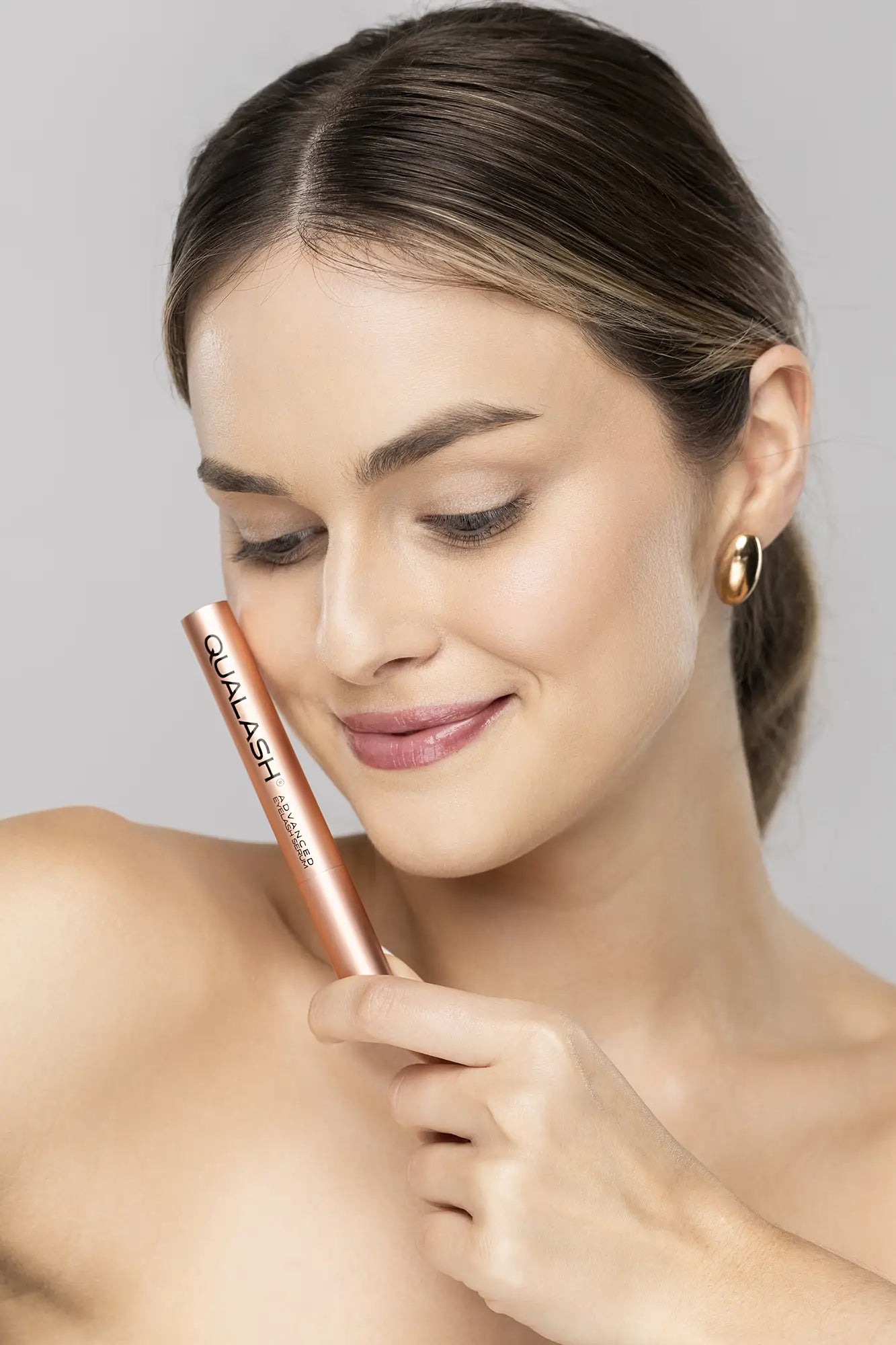 Femme souriante tenant le sérum avancé pour les cils QUALASH