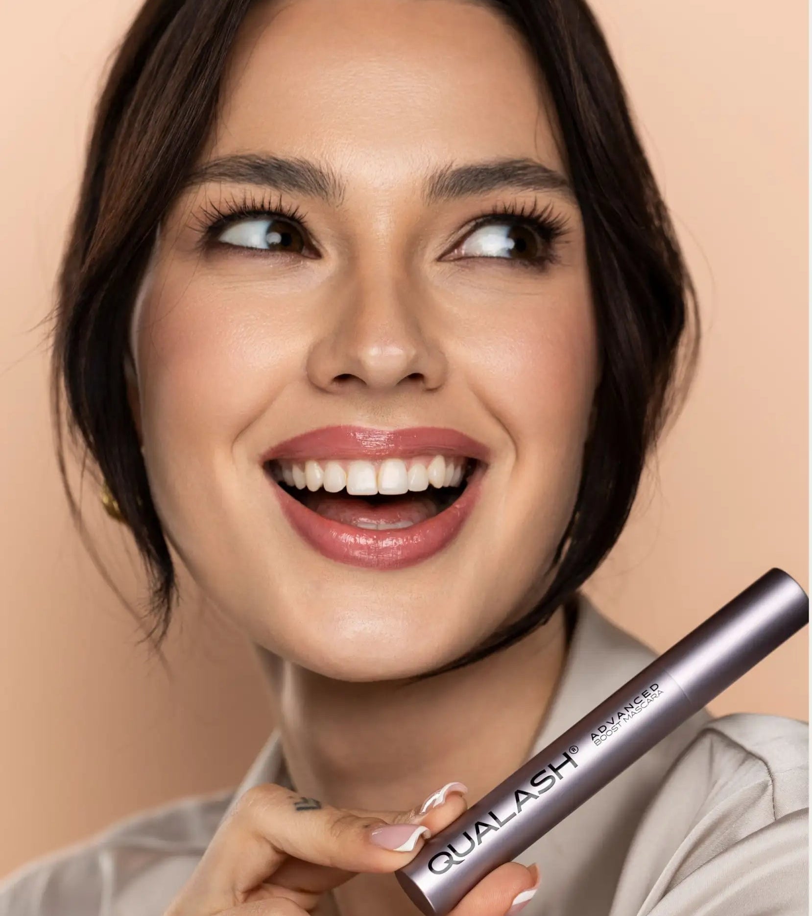 A sleek, metallic silver mascara tube with the brand name ’qualash’ and product line ’advanced’ printed in white lettering.