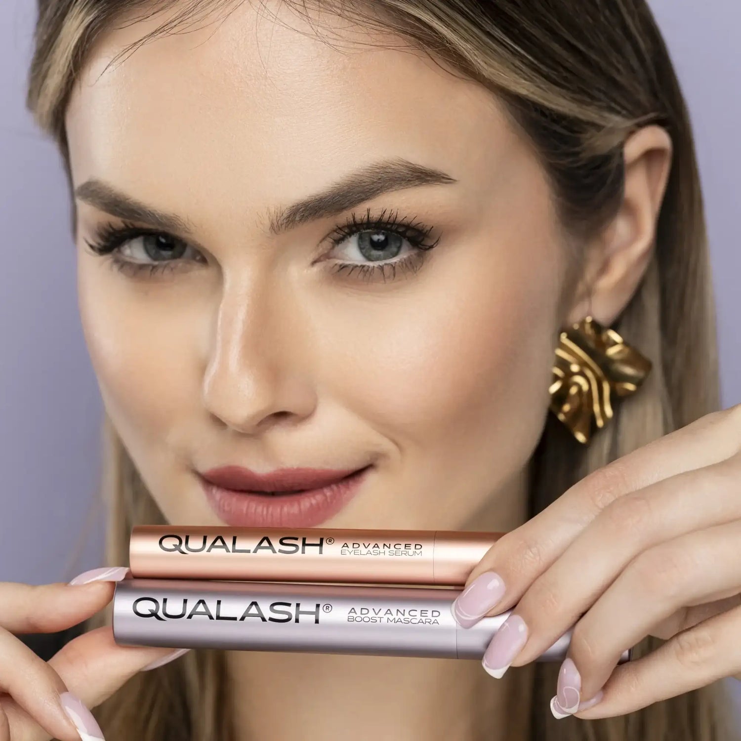 Close-up beauty portrait of a woman holding Qualash eyelash serum and Qualash mascara against a soft neutral background